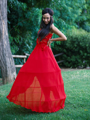 Young happy woman intimate portrait wearing red dress outdoors in a park.