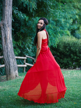 Young happy woman intimate portrait wearing red dress outdoors in a park.