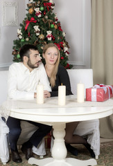 Portrait of a man and woman near the Christmas tree. Wife and husband sitting at the table.