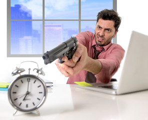 businessman in stress at office computer pointing hand gun to alarm clock project deadline expiring