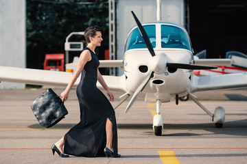 Beautiful woman fashion portrait close to airplane. Filtered ima