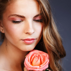 Fototapeta na wymiar Young woman after applying make up posing with pink rose in studio.
