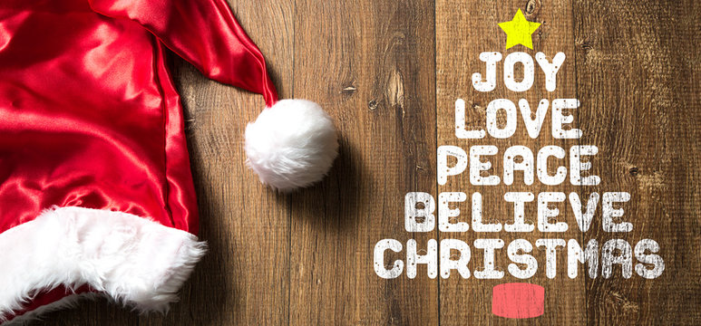 Joy Love Peace Believe Christmas written on wooden with Santa Hat