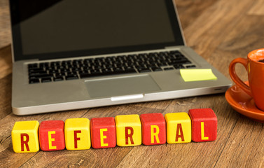 Referral written on a wooden cube in a office desk