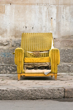 Old Worn Out Yellow Chair Against A Stone Wall