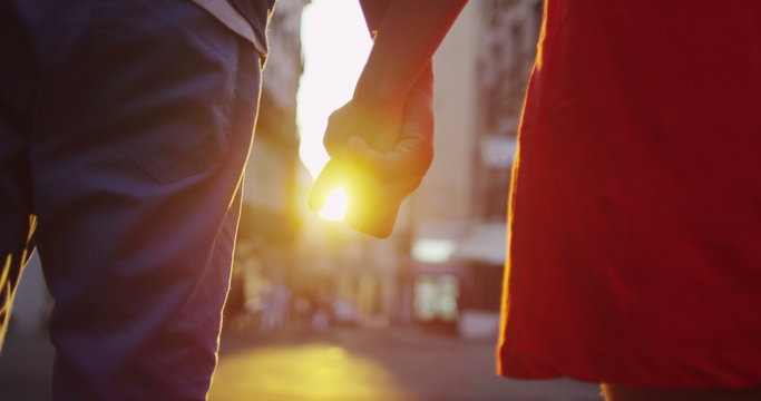  Happy romantic couple holding hands as they walk through city street at sunset. 