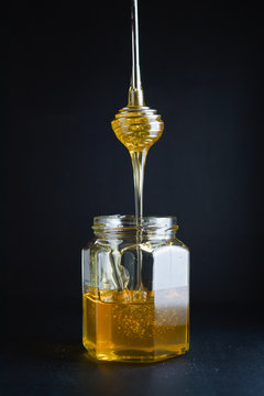 Honey flowing from metal honey dipper into a glass jar