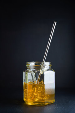 Glass jar with honey and metal honey dipper on dark background