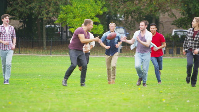  Happy energetic young male friends playing rugby or American football in the park