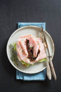 Scandinavian open sandwich with salad, prosciutto cotto, sun-dried tomatoes and thyme on plate. Dark background