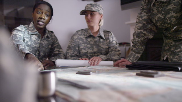  Female military officers in army office, looking at a map and discussing battle strategy. 