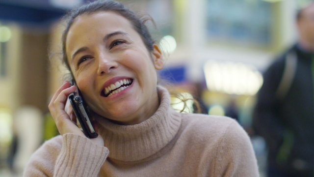  cheerful young woman talking on smart phone in busy train station or airpor