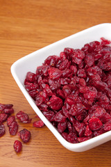Bowl of Dried Cranberries – A white bowl full of dried cranberries. On a wood background.