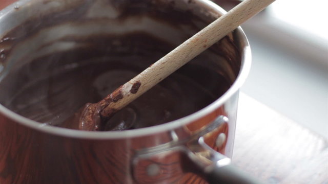Closeup of steaming hot melted chocolate in a pot with a wooden spoon
