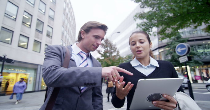  Professional man and woman using computer tablet on a city street