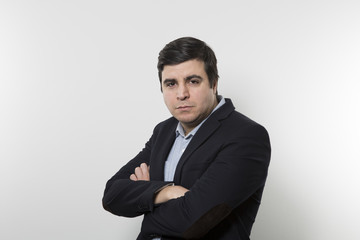 Dark-haired european businessman with a stern look crosses his arms while in front of a gradient background