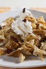 Pancakes cut into strips with a filling of honey, minced walnuts and almonds, raisins and whipped cream, served on a white plate. 