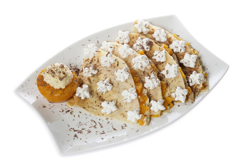 Portion of four pancakes stuffed with vanilla cream and peach, decorated with whipped cream and grated chocolate, served on a white plate. Isolated on white.