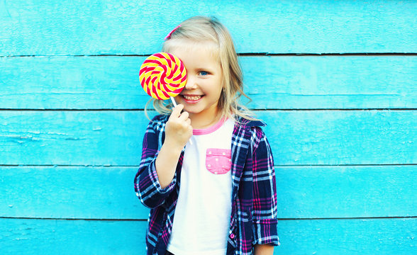 Happy smiling child with sweet lollipop having fun over colorful