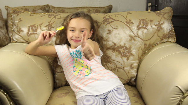 Girl licking candy on a stick in the form of lemon and raises the thumbs up