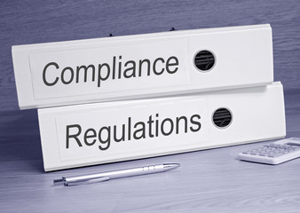 Compliance and Regulations - two binders on desk in the office with pen and calculator