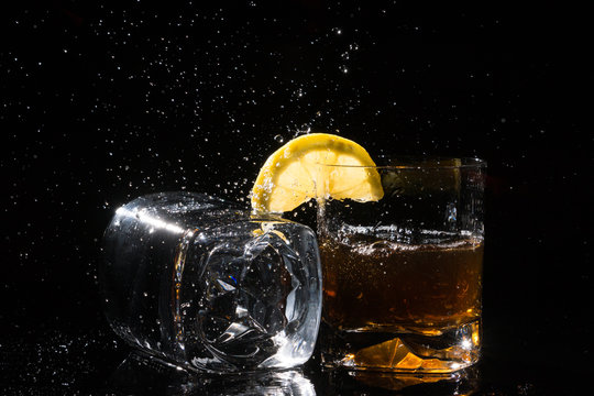 Two hight quality glasses, one lies on side with splashes and other with lemon and splashes on black background.