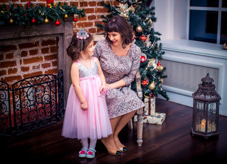 Obraz premium Happy mother with her daughter by the fireplace near Christmas tree
