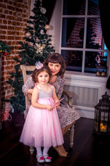 Happy mother with her daughter by the fireplace near Christmas tree