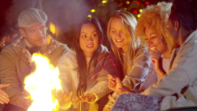  Happy mixed ethnicity friends socializing outdoors in front of fire pit