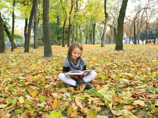 young girl reads a book in the autumn park