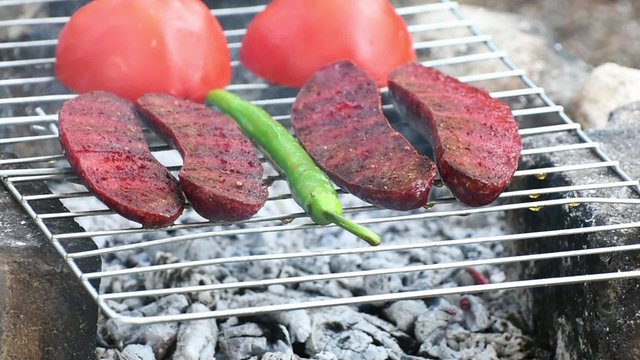 Turkish Sausage ( Sucuk ) cooking on the grill over coals. There are tomato and green pepper on the grill.