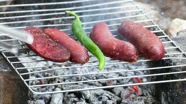 Turkish Sausage ( Sucuk ) cooking on the grill over coals. There are tomato and green pepper on the grill.
