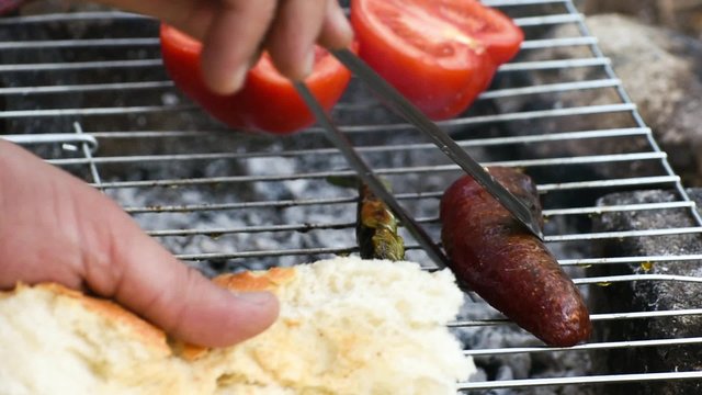 Turkish Sausage ( Sucuk ) cooking on the grill over coals. There are tomato and green pepper on the grill.
