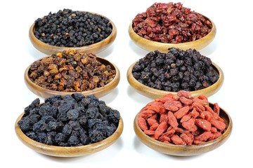 Auswahl getrockneter Beeren (Aronia, Sanddorn, Goji, Berberitzen, Schisandra, Hollunder) in Olivenholzschalen isoliert auf weißem Hintergrund