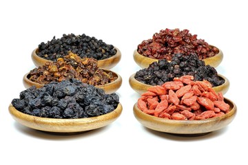Auswahl getrockneter Beeren (Aronia, Sanddorn, Goji, Berberitzen, Schisandra, Hollunder) in Olivenholzschalen isoliert auf weißem Hintergrund