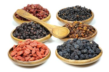 Auswahl getrockneter Beeren (Aronia, Sanddorn, Goji, Berberitzen, Schisandra, Hollunder) in Olivenholzschalen isoliert auf weißem Hintergrund