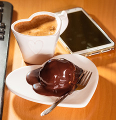 Cup of coffee and chocolate cake next to computer.