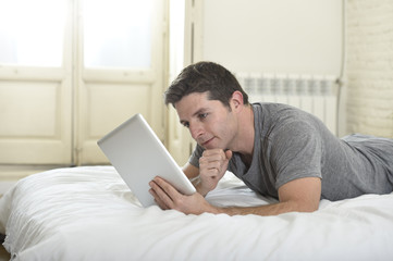 young attractive man lying on bed or couch enjoying social networking using digital tablet computer internet at home