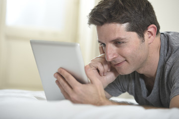 young attractive man lying on bed or couch enjoying social networking using digital tablet computer internet at home