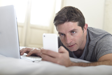 young attractive man lying on bed or couch using mobile phone and computer laptop internet addict