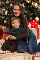 Portrait of a happy mother embracing her cute little son in front of the Christmas tree