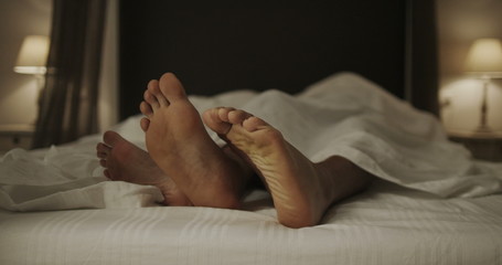 Happy dancing feet of funny couple in bed together