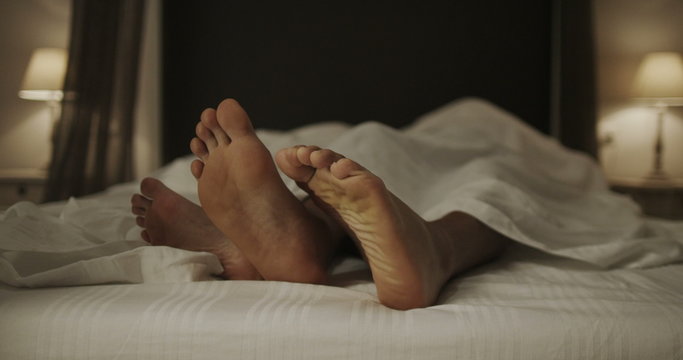 Happy dancing feet of funny couple in bed together