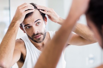 Concentrated man looking at his hair in mirror