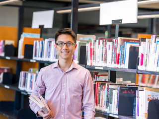 Happy male student holding books at the library