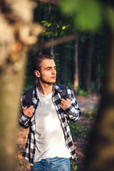 Portrait of young handsome man with backpack wanderer walk in the woods