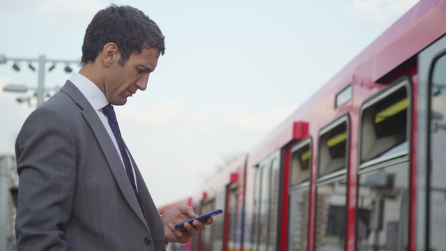  Businessman texting on his smartphone as train comes into the station.