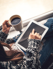 Soft photo of woman In the armchair with tablet and cup of coffee in hands, ripped jeans