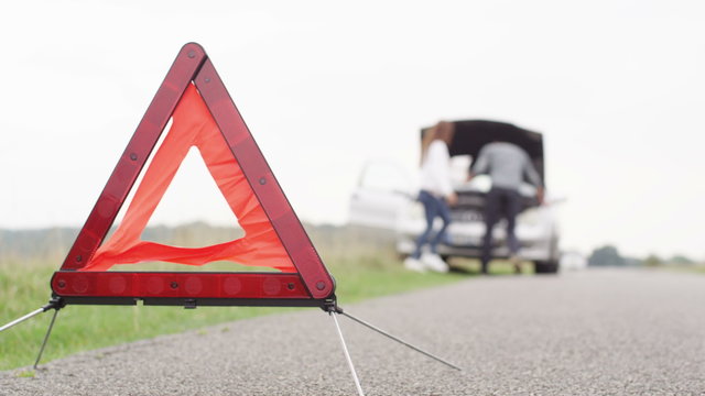  Couple trying to fix broken down car with hazard triangle in the foreground
