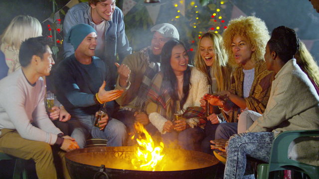  Happy mixed ethnicity friends socializing outdoors in front of fire pit